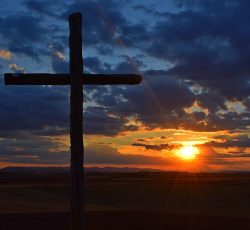 a cross on a hill with a sunset in the background